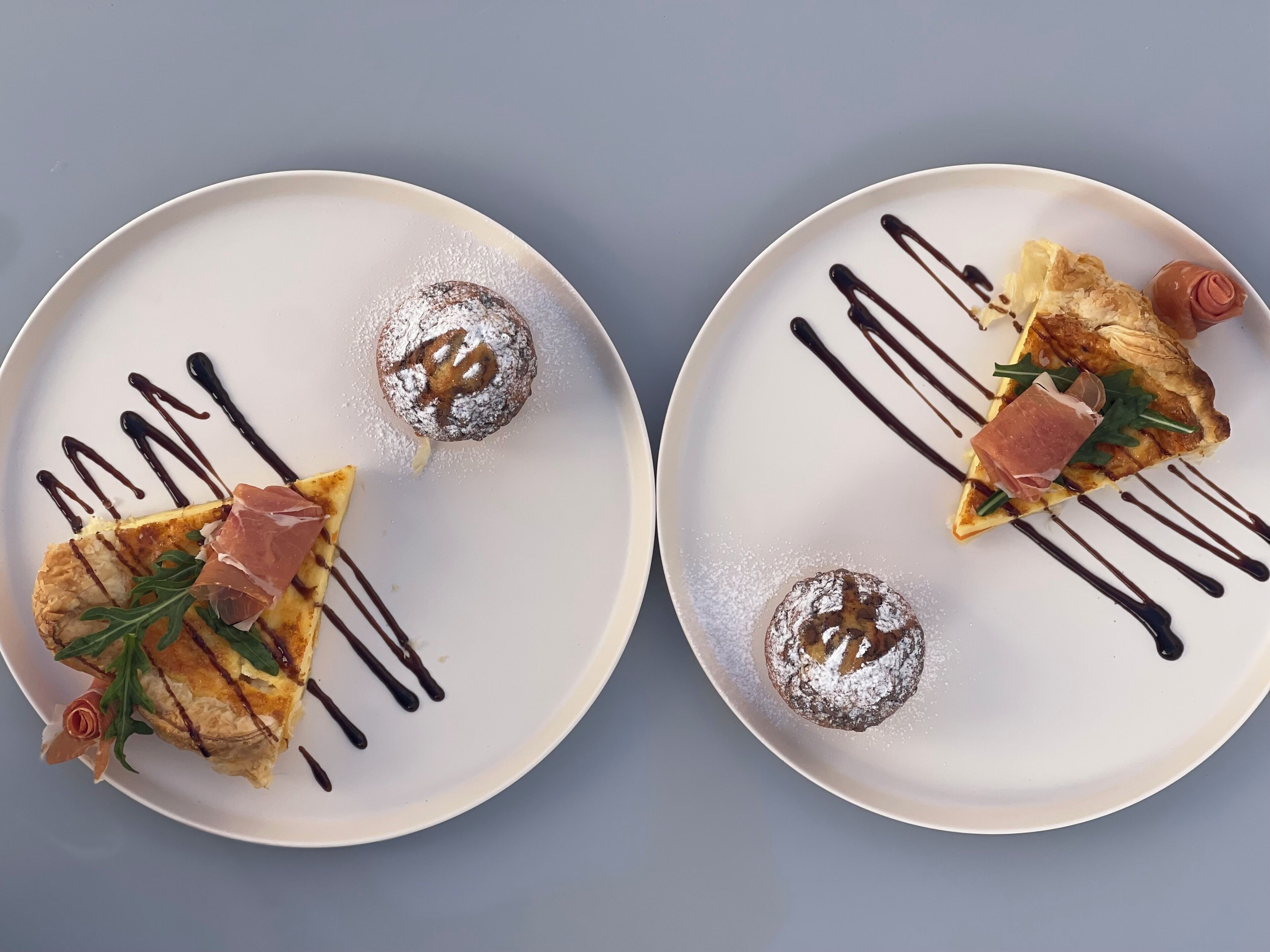 Two plates with food, each with a dusting of powdered sugar and chocolate drizzle.