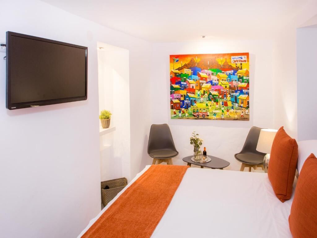 Habitació d'hotel amb un llit, dues cadires, una taula petita amb una planta i un mural colorit a la paret.