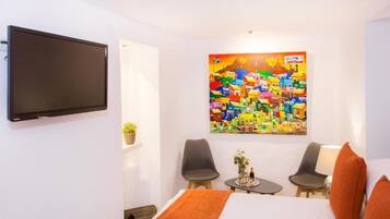 Habitació d'hotel amb un llit, dues cadires, una taula petita amb una planta i un mural colorit a la paret.
