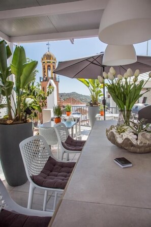 Une terrasse avec des sièges extérieurs, des plantes en pot et une vue sur le clocher d’une église.