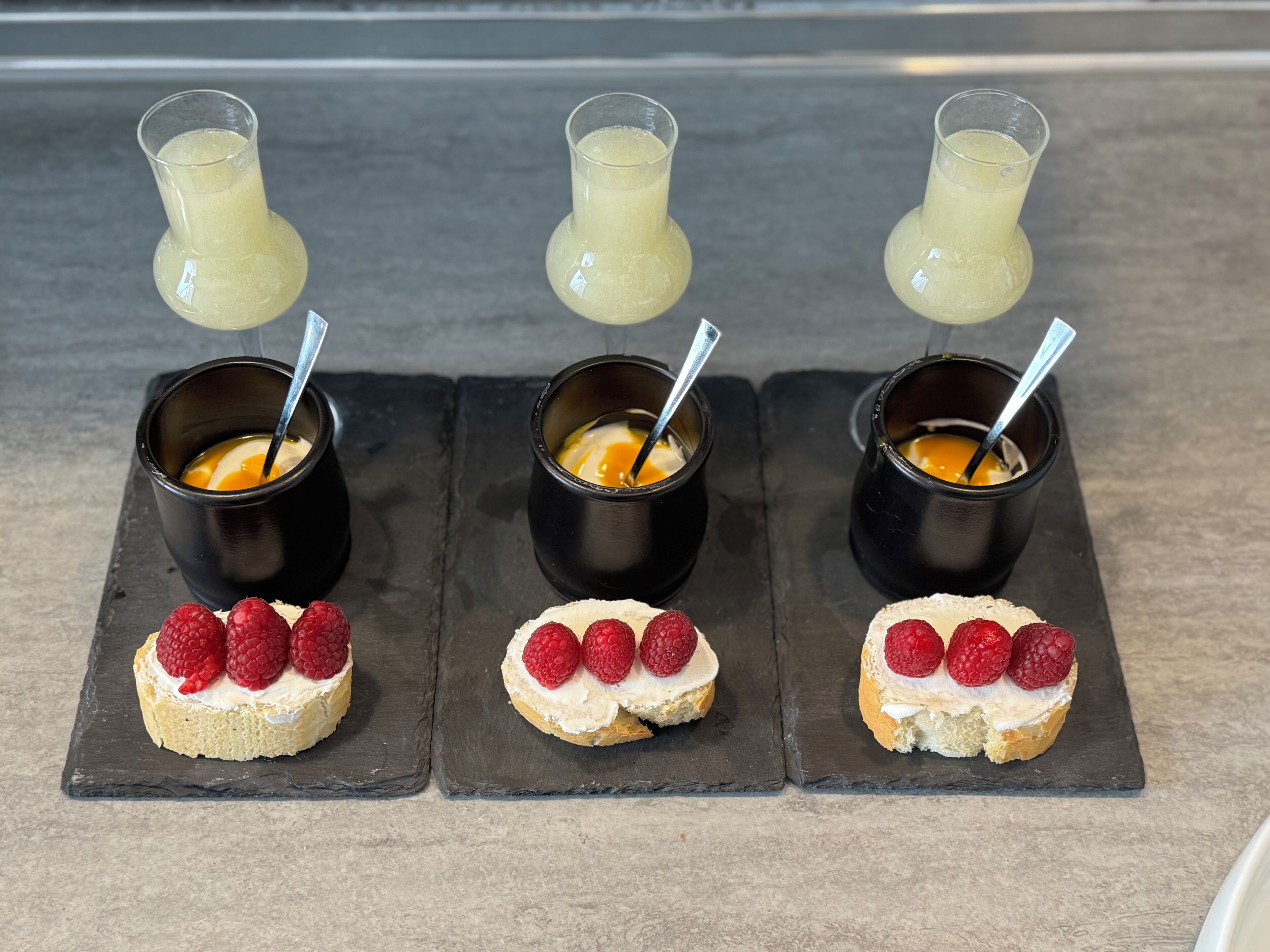 Three dessert plates with cream and raspberries, each paired with a glass of a yellow beverage.