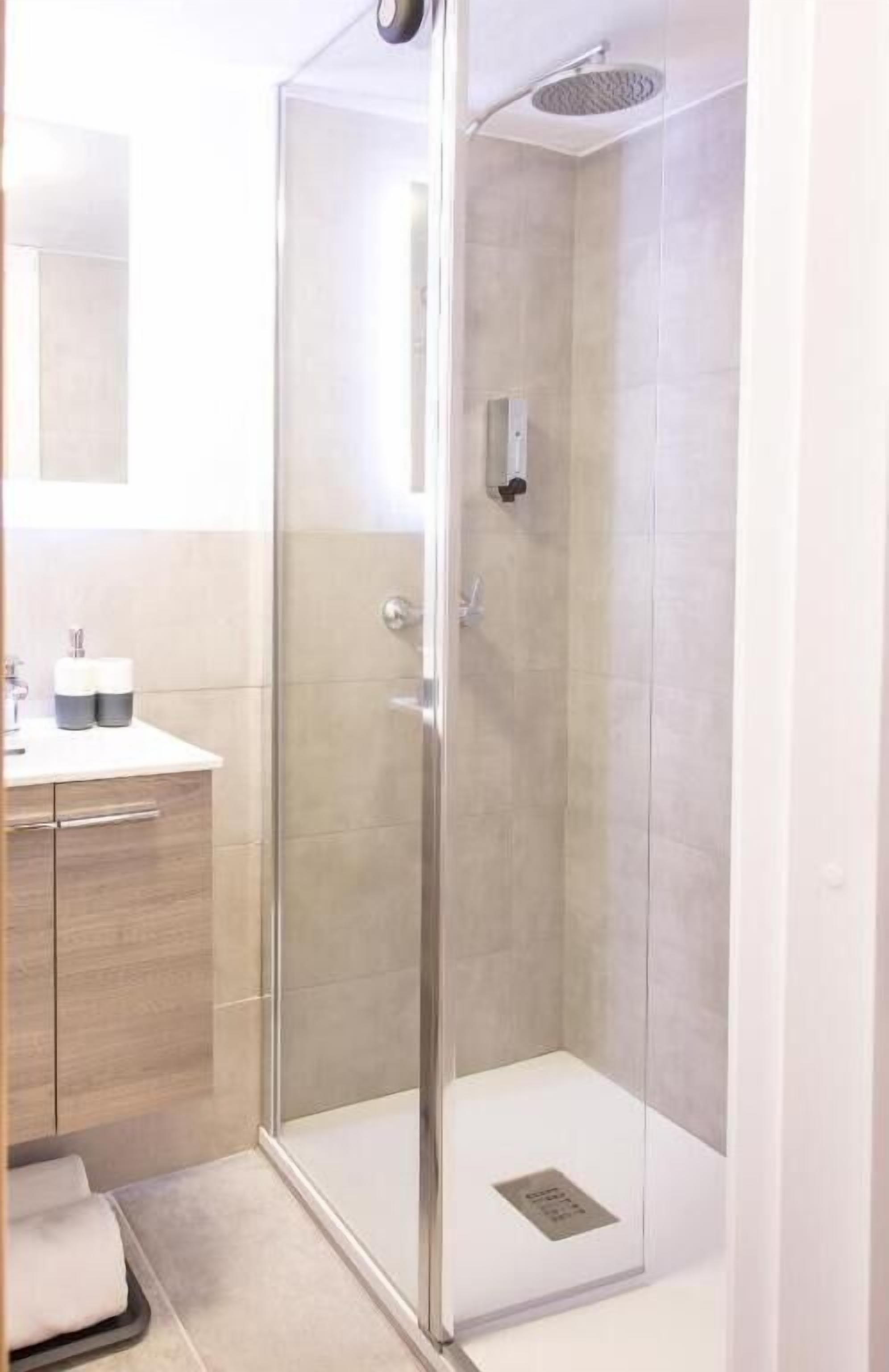 Un baño moderno con ducha de vidrio, tocador de madera y espejo sobre el lavabo.
