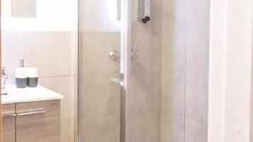Un baño moderno con ducha de vidrio, tocador de madera y espejo sobre el lavabo.