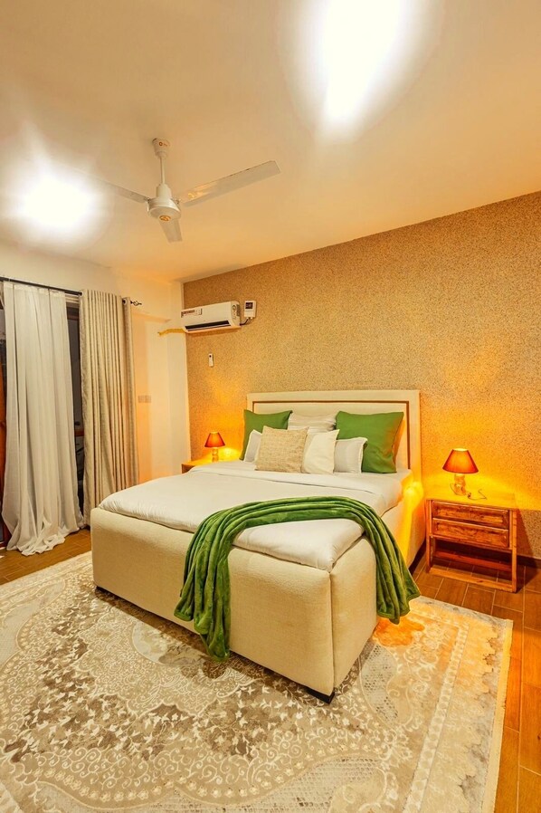 Une chambre à coucher comprenant un lit, un ventilateur de plafond, un appareil de climatisation, une lampe de chevet et un tapis à motifs.