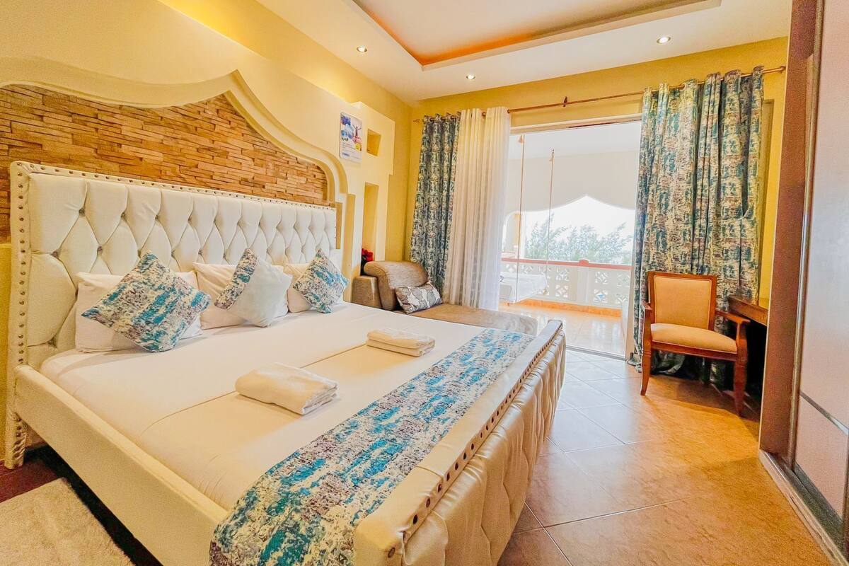 Um quarto espaçoso com uma cama grande, uma cabeceira de madeira e uma varanda com cortinas.