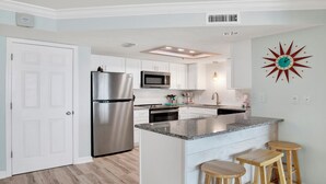 Una cocina moderna con armarios blancos, electrodomésticos de acero inoxidable, encimera de granito y un reloj de pared original.