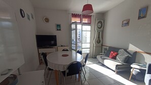A living room with a dining area, a sofa, a TV, and a clock on the wall. - 3-bedroom house, sleeps 6, near station, Sète, WIFI (Sète)