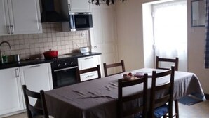 Een keuken met witte kasten, een fornuis en een magnetron. Er is een eettafel met stoelen en een kroonluchter.