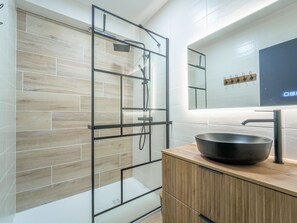 Ein modernes Badezimmer mit einer gläsernen Duschkabine, einem Holzwaschtisch mit schwarzem Becken und einem Spiegel mit digitaler Anzeige.