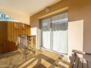 Ein Balkon mit Korbstuhl, Holztisch und einer Schiebetür aus Glas.