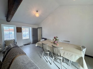 A dining area with a long table, white chairs, and a vase of flowers.