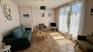A living room with a sofa, a TV, a small table, and a window with curtains. - Carnac House 4 Rooms, Garden, Pets Allowed (Carnac)
