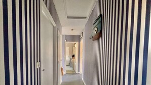 A hallway with striped walls and a carpeted floor, leading to a room with a bed and a dresser. - Carnac House 4 Rooms, Garden, Pets Allowed (Carnac)