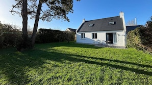 A single-story house with a white exterior and dark roof, surrounded by a well-maintained lawn and a large tree to the left. - Carnac House 4 Rooms, Garden, Pets Allowed (Carnac)