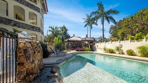 A swimming pool with a stone wall, lounge chairs, and a gazebo. - Makai Hawaiian for direction towards the ocean (Mount Coolum)