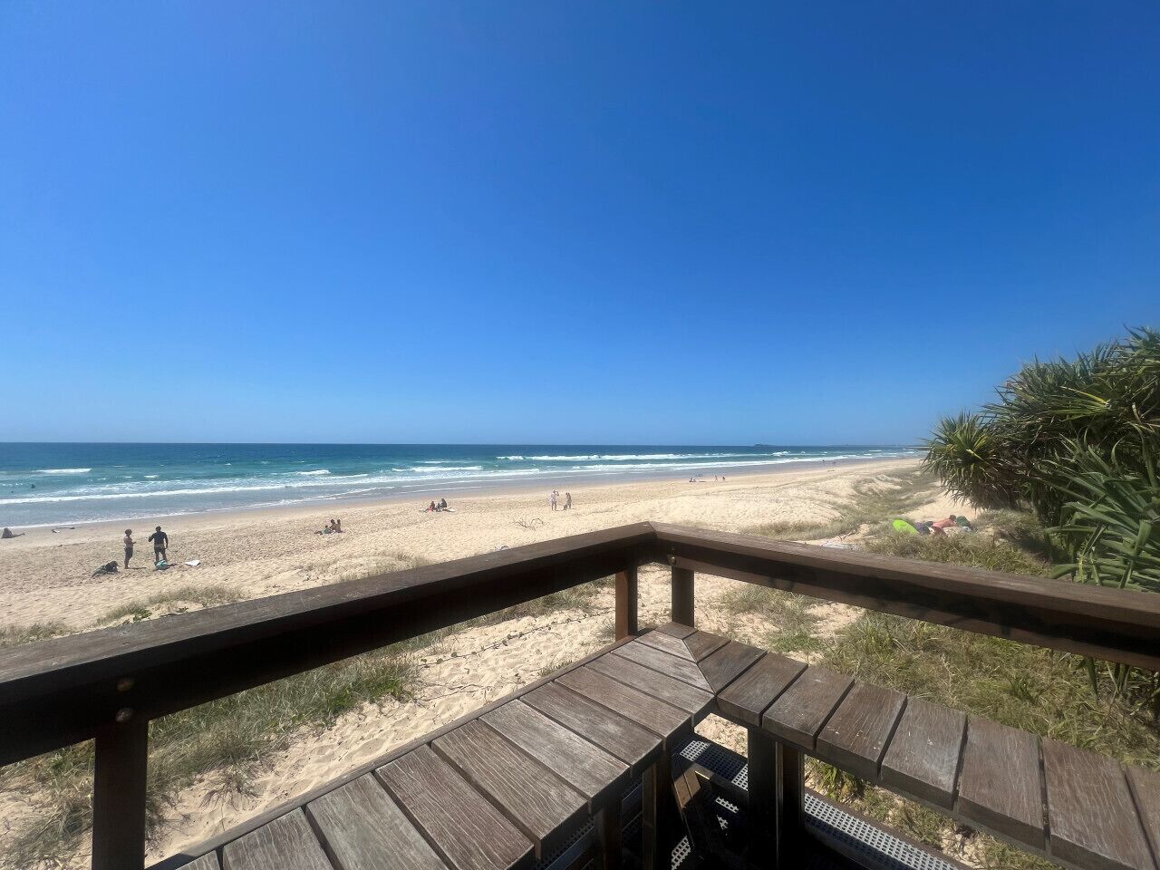 A beach view from a wooden deck with a clear sky.