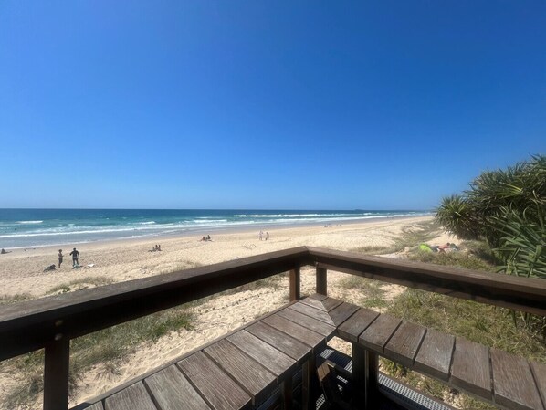 Vista de la playa desde una terraza de madera con cielo despejado.