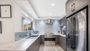 A modern kitchen with a stainless steel refrigerator, a gas stove, and a built-in oven. - Makai Hawaiian for direction towards the ocean (Mount Coolum)