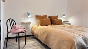A bedroom with a bed, two bedside tables with lamps, a chair with towels, and a wooden floor. - The Sorbier house, Provence (Maillane)