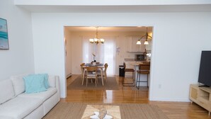 A modern living room with a sofa, a dining area with a table and chairs, and a kitchen with cabinets and a microwave.