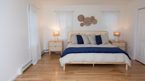 A bedroom with a wooden bed, two bedside tables with lamps, a decorative wall piece, and a window with blinds.