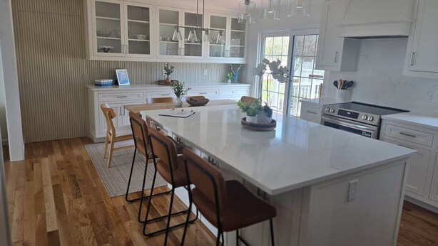 A modern kitchen with a large island, white cabinetry, and a view to the outside.