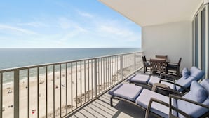 A balcony with wicker furniture, a view of the beach, and a clear sky.