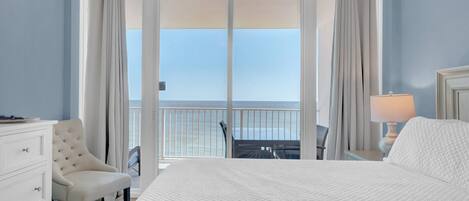 Ein Hotelzimmer mit einem großen Bett, einem Sessel, einem Schreibtisch und Meerblick durch eine Schiebetür.