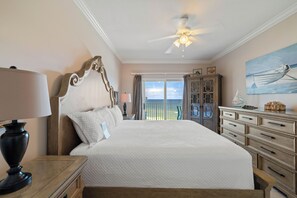 Une chambre spacieuse avec un grand lit, un ventilateur de plafond, une table de chevet, une commode et une vue sur l’extérieur.