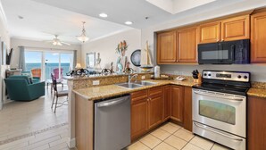 A modern kitchen with granite countertops, wooden cabinets, a stainless steel dishwasher, a double oven, and a microwave. - Seawind 902 by Liquid Life (Gulf Shores)