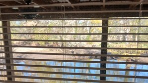 Une pièce avec des stores horizontaux, un plafond apparent avec des poutres en bois et une vue sur une étendue d’eau.