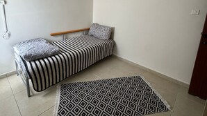 Habitació petita i ordenada, amb un llit, una catifa amb dibuixos i un quadre penjat a la paret.