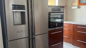 Una cuina amb un frigorífic d'acer inoxidable, forn integrat, armaris de fusta i una finestra que deixa entrar llum natural.