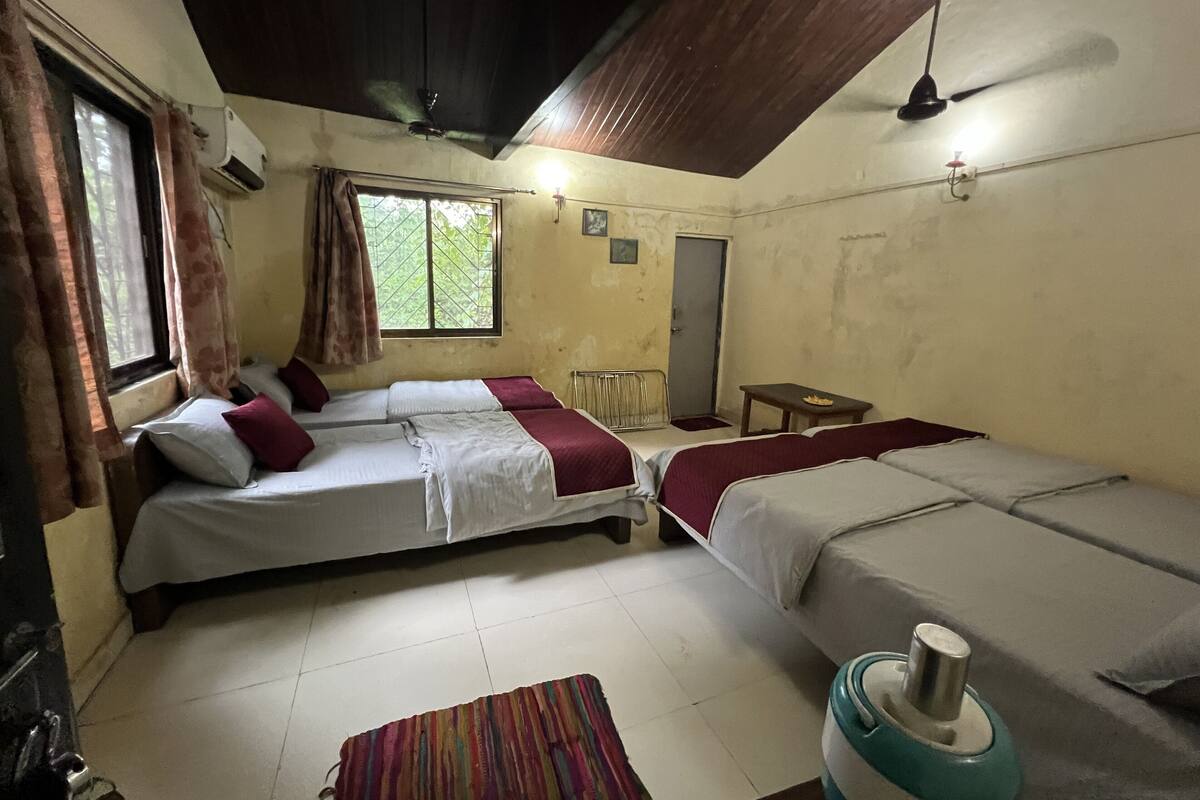 Une chambre avec deux lits, une fenêtre avec des rideaux, un radiateur, une petite table et un ventilateur de plafond.