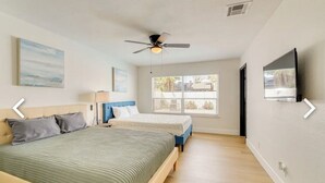 Quarto com cama, ventoinha no teto, janela e televisão na parede.