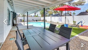 Um alpendre coberto com piscina, mobiliário de exterior e um guarda-sol vermelho.