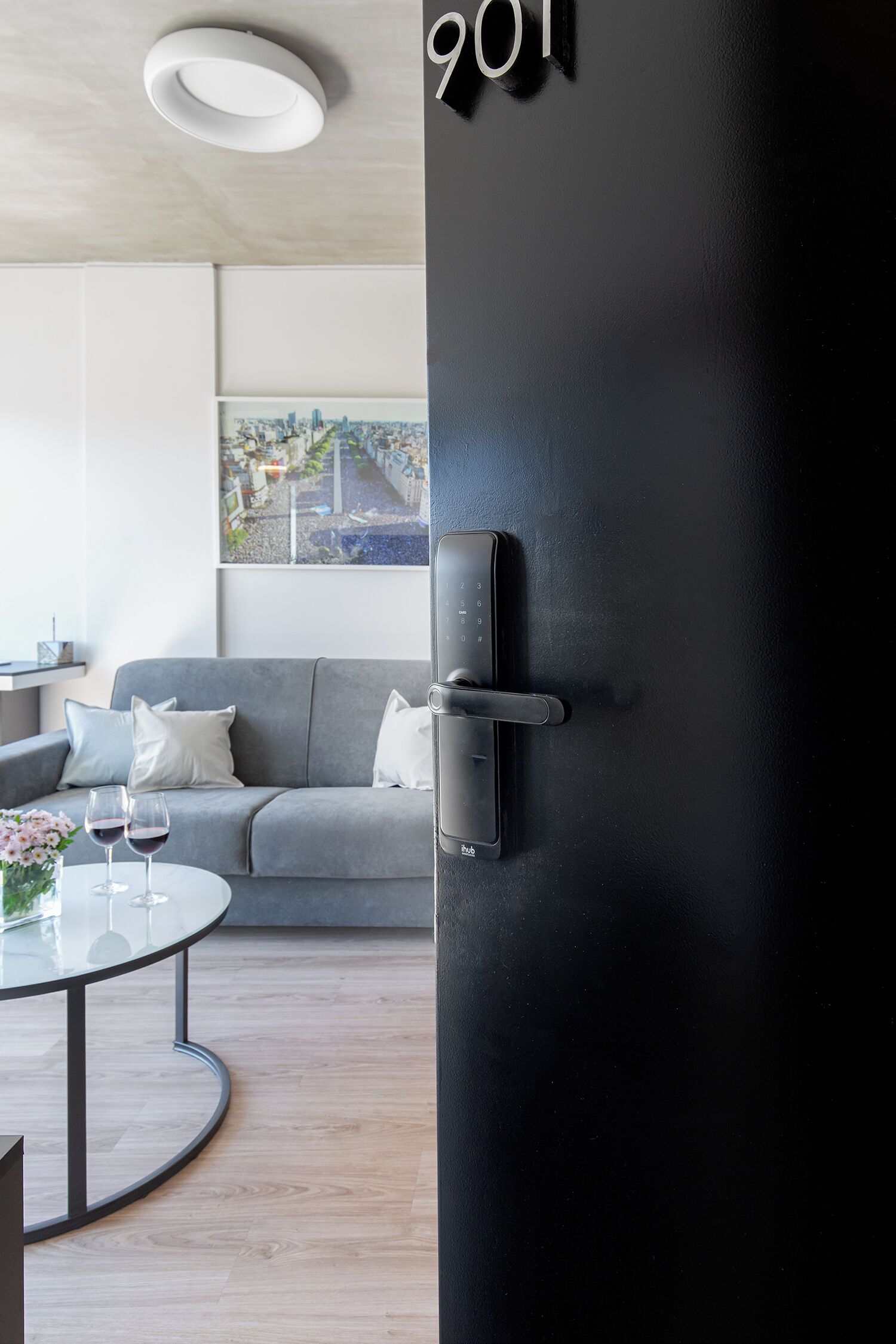 Ett modernt rum med en grå soffa, ett glasbord med vinglas och en svart dörr med ett digitalt lås.