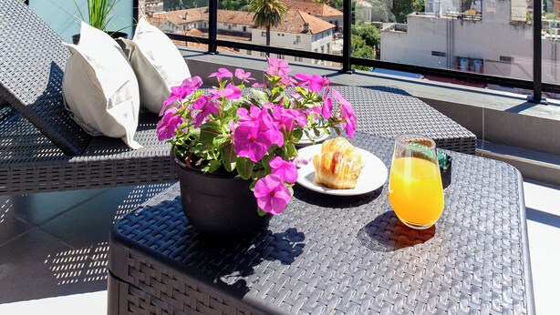 Een balkon met uitzicht over de stad, een tafel met een drankje, bloemen en een bord eten.