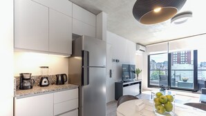 Een moderne keuken met een roestvrijstalen koelkast, een koffiezetapparaat en een blender op het aanrecht. Er staat een eettafel met een vaas vol appels.