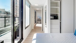 Een moderne hotelkamer met een groot bed, uitzicht op de stad via een balkon en een bureau met stoel.