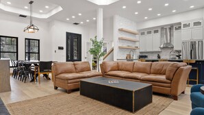 A spacious living room with a large brown leather sofa, a black coffee table, and a dining area with chairs and a table.