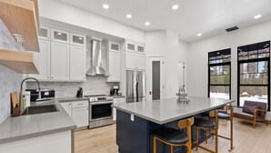 A modern kitchen with white cabinetry, stainless steel appliances, and a large island with bar stools.