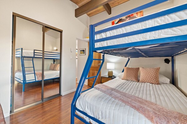 A bunk bed room with a wooden ladder, a sliding door, and a bedside table with a lamp.