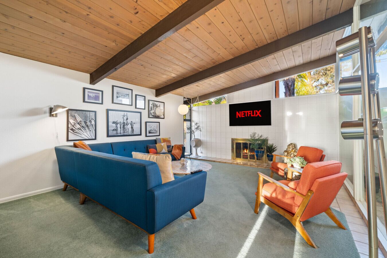 Ein modernes Wohnzimmer mit einem blauen Sofa, orangefarbenen Sesseln, einem Kamin und einem Netflix-Schild.