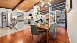 A modern kitchen with stainless steel appliances, a dining area with a wooden table and green chairs, and a view of the outdoors through a glass door. - Golden Hour Bliss: Pool, Hot Tub & Firepit (La Mesa)