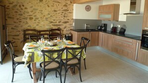 Un espace repas agrémenté d’un mur en pierre, de poutres apparentes en bois au plafond et d’une cuisine équipée d’appareils électroménagers modernes.