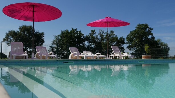 Une piscine aux eaux cristallines, dotée de chaises longues et de deux grands parasols.