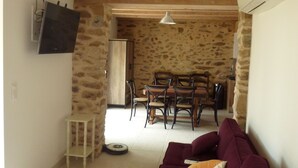 Un salon chaleureux avec un canapé violet, un coin repas avec une table et des chaises en bois, et un mur en pierre.