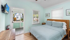 A bedroom with a bed, wooden headboard, and a view of a house through a door. - ~CONCH COTTAGES~ Enjoy your next island vacation with friends right here! (Key West)