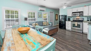 A spacious kitchen with white cabinets, a black refrigerator, and a wooden dining table with a bowl. - ~CONCH COTTAGES~ Enjoy your next island vacation with friends right here! (Key West)